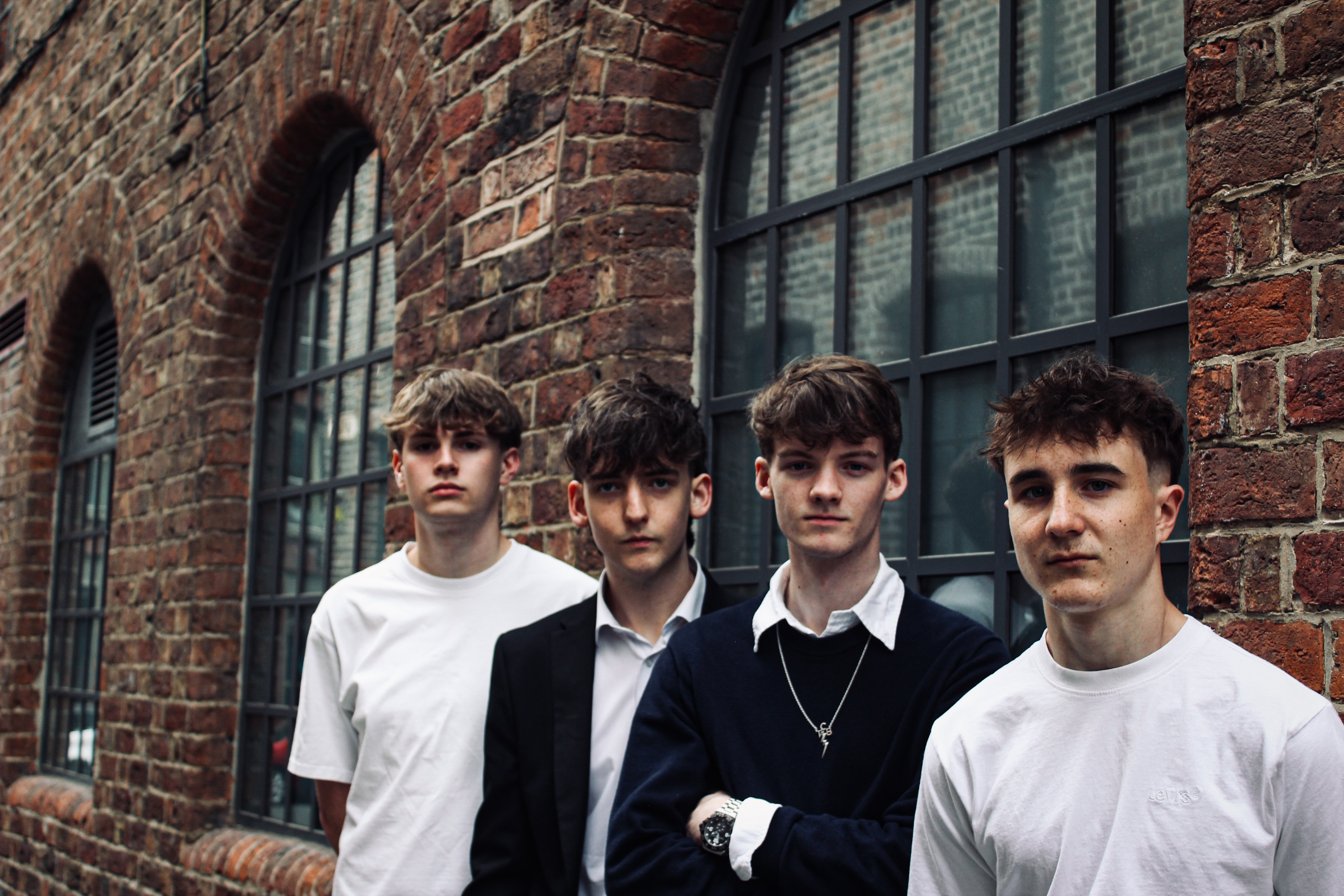 Band EVERYMAN posing against red brick warehouse wall for the unsigned guide spotlight July 2026 feature